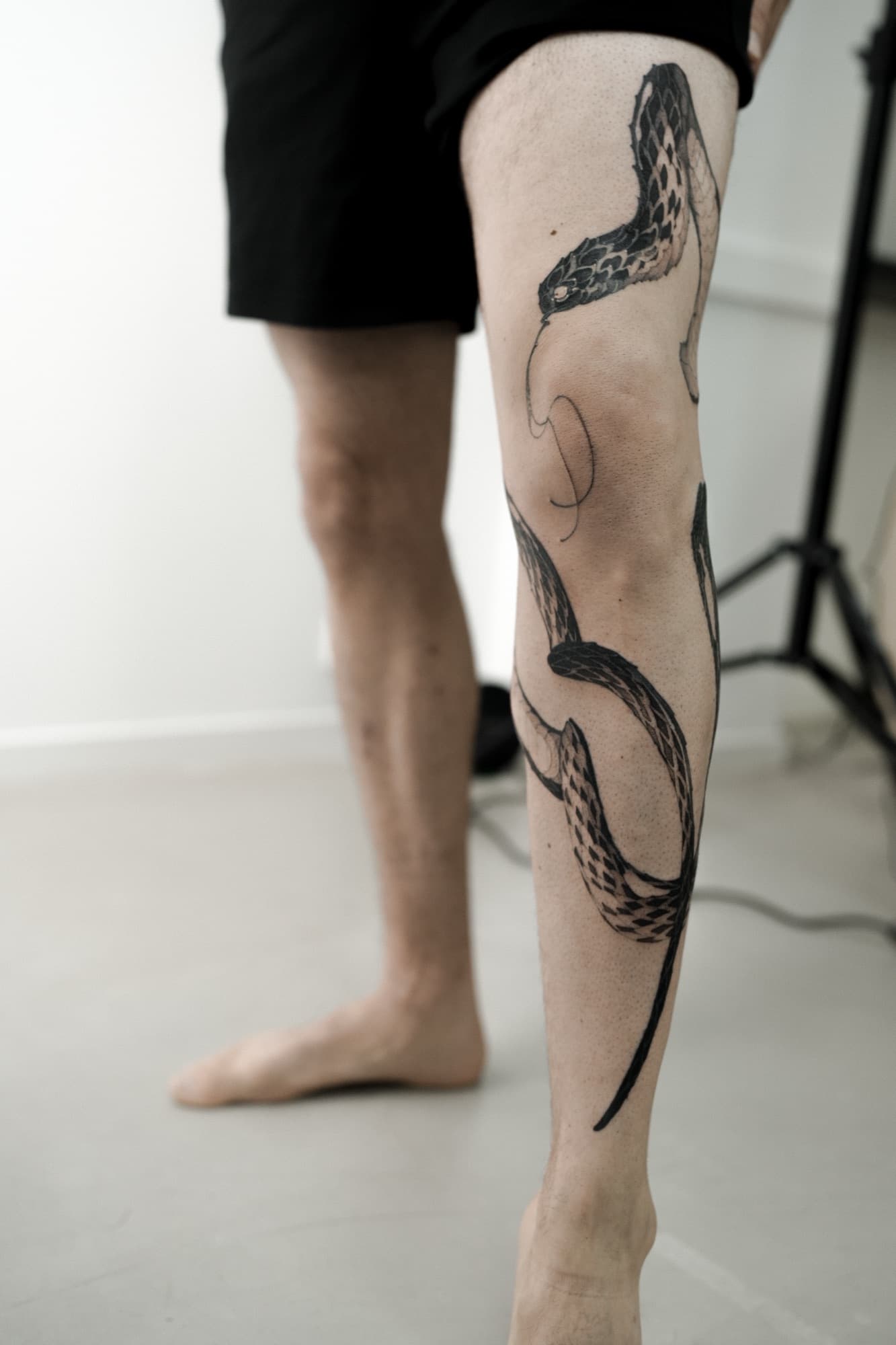 Fine-line black snake tattoo winding down the lower leg